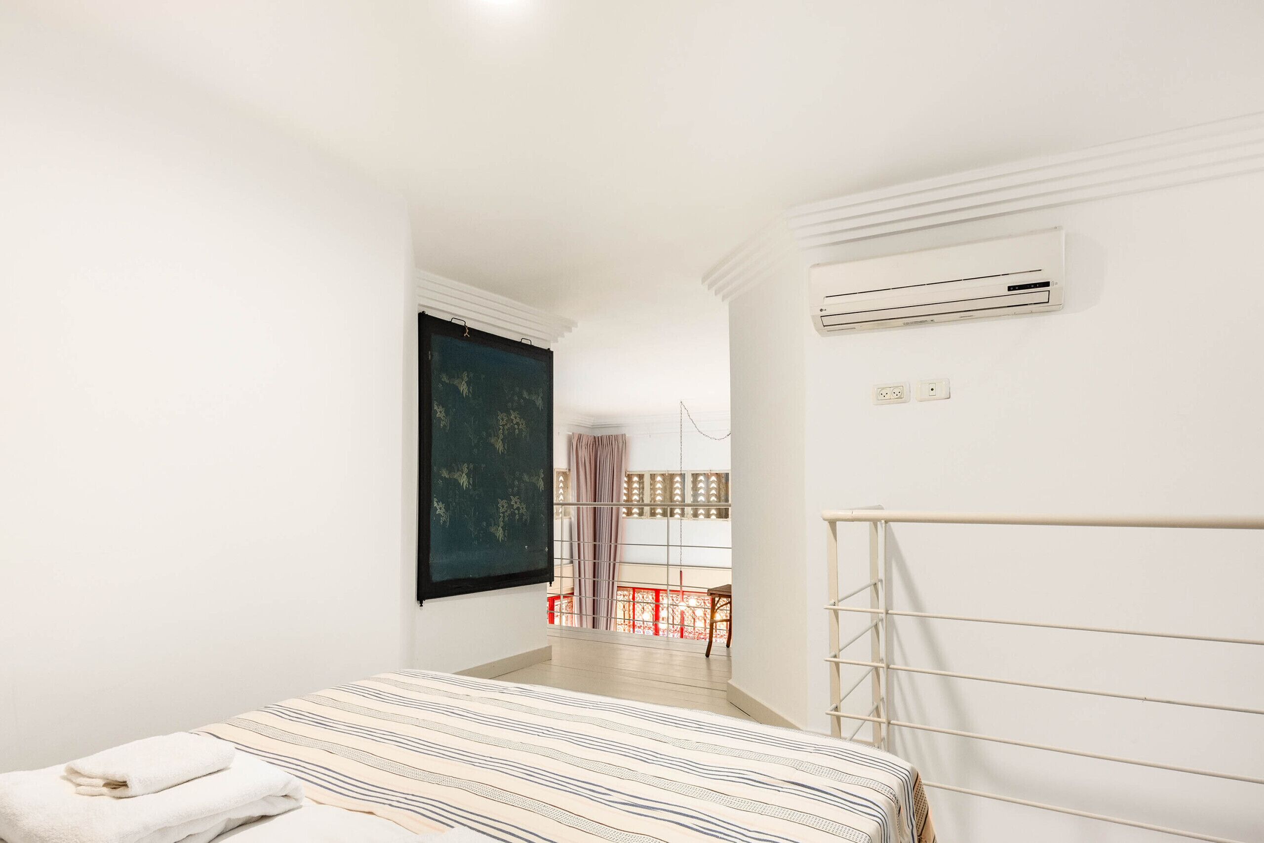 Une chambre à coucher avec un lit, une fenêtre, un appareil de climatisation et une vue sur un balcon.