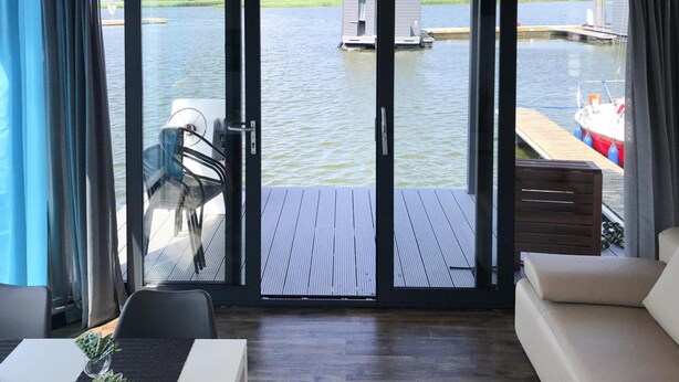 Ein Zimmer mit einer großen Schiebeglastür, die auf eine Holzterrasse mit Blick auf einen See mit Anlegestegen und Booten führt.
