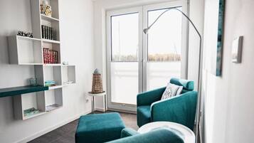 Una sala de estar moderna con un sofá color aguamarina, una mesa redonda blanca y una estantería con diversos objetos.