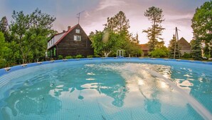 Ein Swimmingpool mit blau gefliestem Deck, umgeben von Bäumen und einem Gebäude mit Schrägdach.
