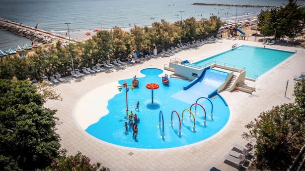 A pool area with a water slide, lounge chairs, and a view of the sea. - Bungalow in Caorle With Garden Furniture (Caorle)