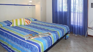 A bedroom with a bed, a nightstand, a window with blue curtains, and a wall-mounted shelf with a lamp. - Villas Nautilus in Bibione With Pool (San Michele al Tagliamento)