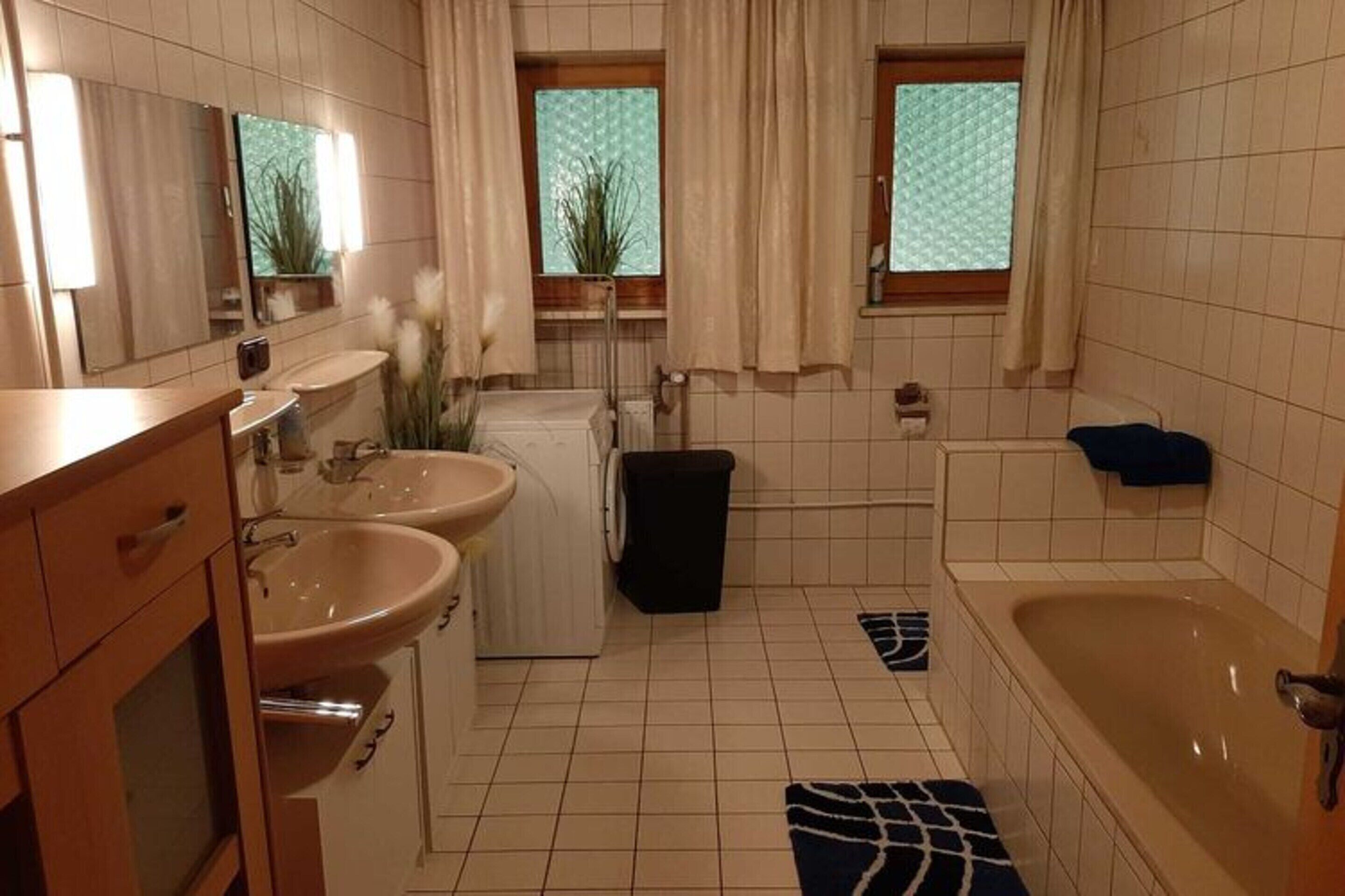 A bathroom with two sinks, a bathtub, a mirror, and a window with curtains.