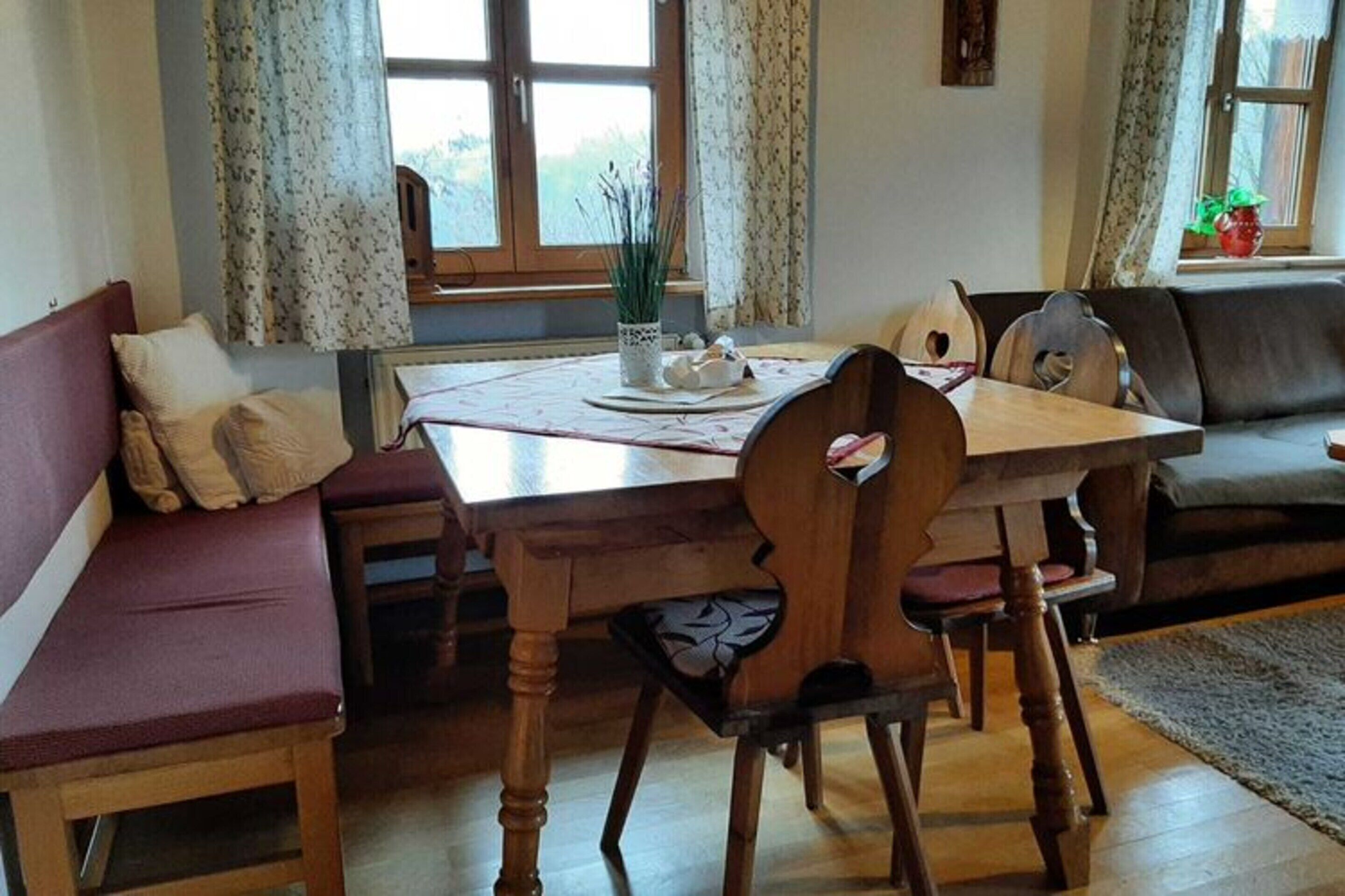 Een gezellige woonkamer met een houten eettafel, een met kussens beklede zitting en een bank.