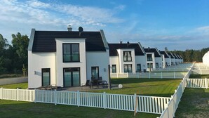 Une rangée de maisons modernes, toutes blanches, avec des toits sombres, chacune dotée d’une terrasse et d’une clôture en bois peinte en blanc.