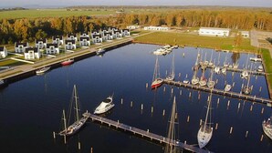 Un port de plaisance où sont amarrés de nombreux bateaux, une rangée de bâtiments blancs et, au fond, une zone herbeuse.