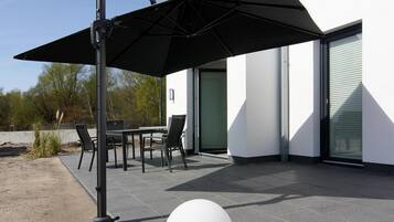 En udendørs terrasse med et bord, stole og en sort parasol, samt en hvid, rund genstand.