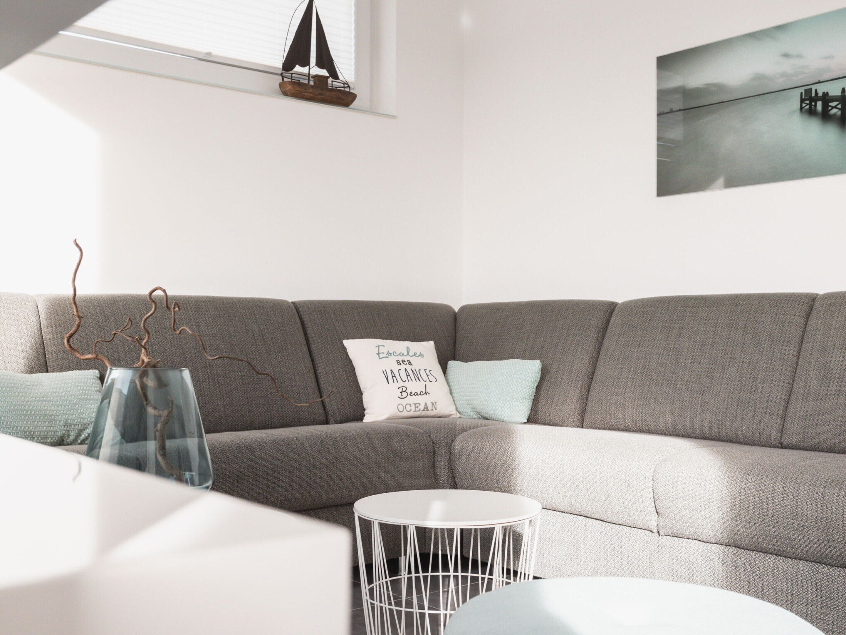 A modern living room with a grey sectional sofa, a white round coffee table, and a decorative sailboat model on a shelf.