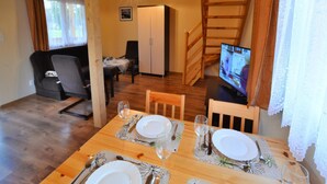 Ein Essbereich mit Holztisch, gedeckt für vier Personen, einer Couch und einem Fernseher im Hintergrund.
