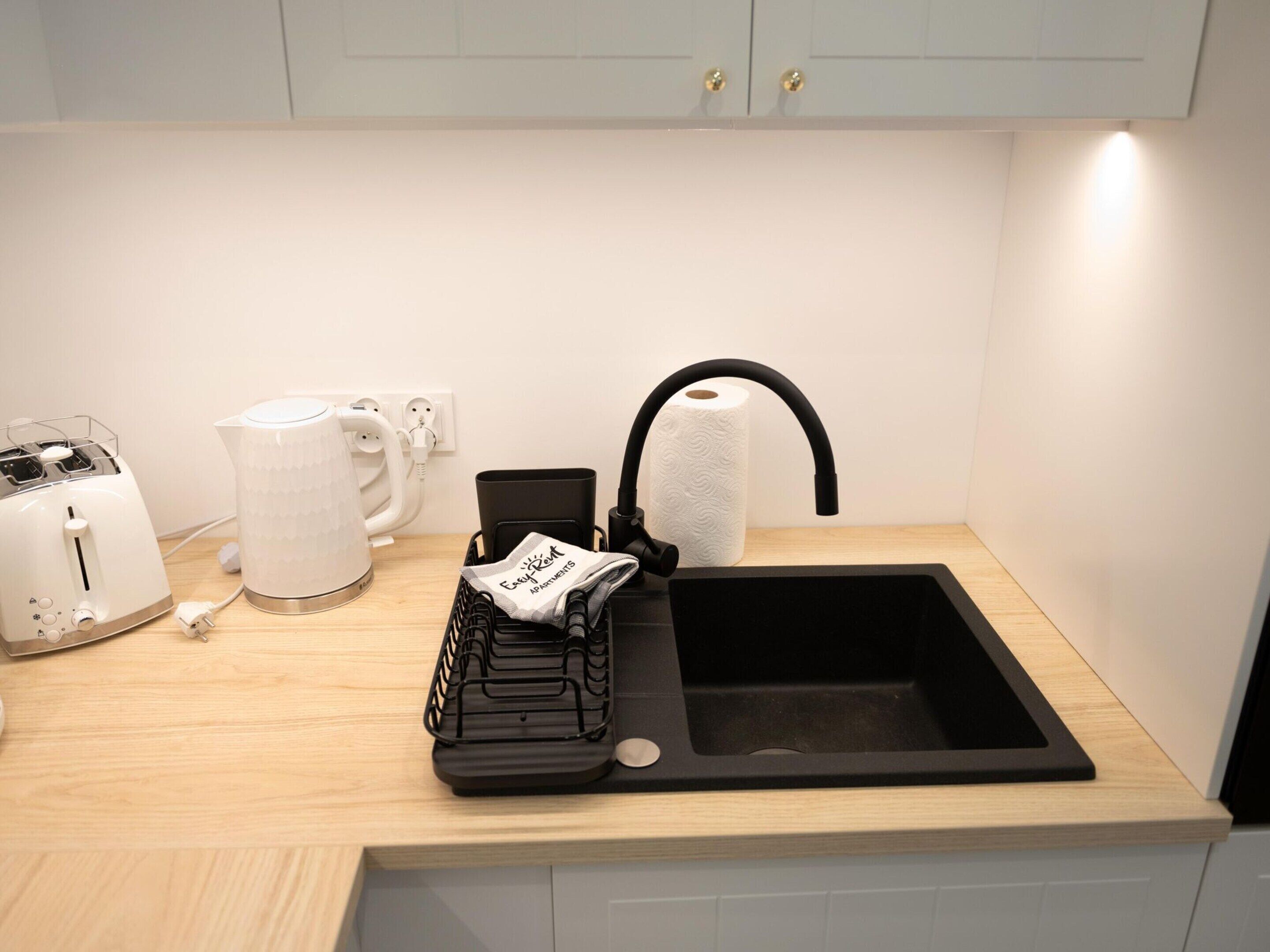 A kitchen with a black sink, a white kettle, a toaster, and a coffee maker.