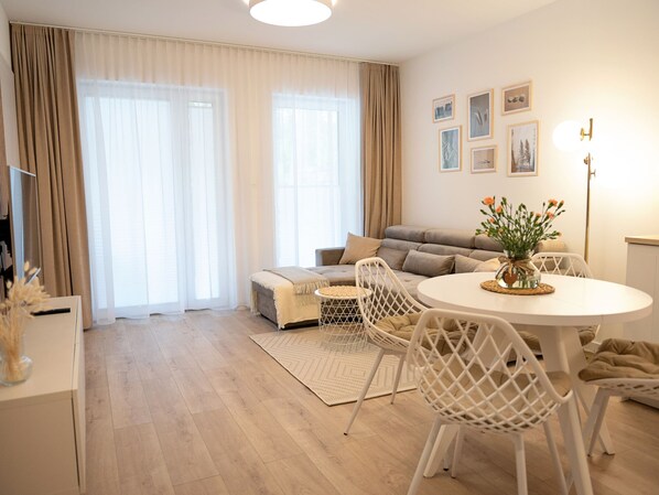 Una sala de estar moderna con un sofá, una mesa de comedor con sillas y un ventanal con cortinas.