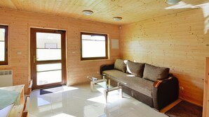 A wooden cabin interior with a sofa, a glass coffee table, and a door leading outside. - Cottage in Sarbinowo Near Baltic Sea Beach (Mielno)