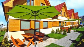 A row of wooden cabins with red roofs, outdoor seating, and green umbrellas. - Cottage in Sarbinowo Near Baltic Sea Beach (Mielno)