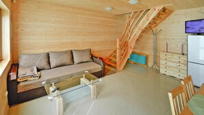 A wooden interior with a sofa, a glass coffee table, a wooden staircase, a TV, and a refrigerator. - Cottage in Sarbinowo Near Baltic Sea Beach (Mielno)