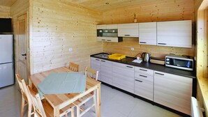 A compact kitchen with wooden walls, a dining table with chairs, and basic appliances. - Cottage in Sarbinowo Near Baltic Sea Beach (Mielno)