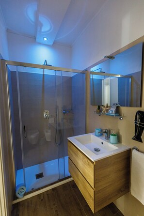 Un baño moderno con ducha envuelta en vidrio, tocador de madera con lavamanos y un espejo grande sobre el tocador.