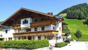 A two-story building with a balcony, surrounded by greenery and a hilly landscape. - Apartment in Filzmoos Near Ski Amade (Filzmoos)