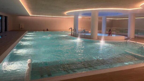 Una piscina interior con varias pistas de natación, una fuente central y una zona de estar con barandilla.