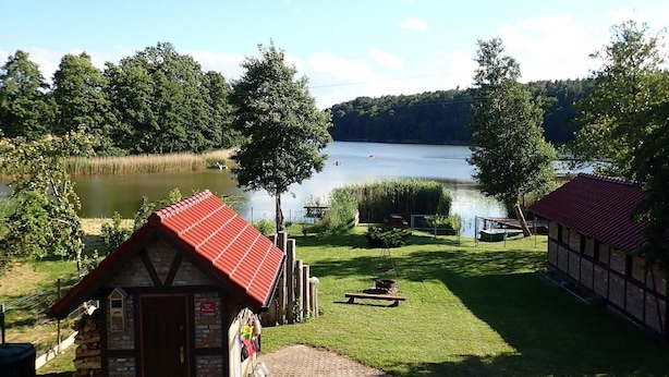 A lakeside cabin with a red roof, a picnic table, and a small shed. - Holiday Home in Kolczewo With Lake Access (gmina Wolin)