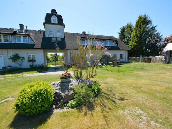 A two-story house with a prominent tower-like structure on the roof, a well-maintained lawn, and a stone feature with a wheel.