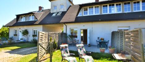 A two-story house with a large front yard, a wooden fence, and a patio area with outdoor furniture.