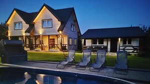 Une maison à deux étages dotée d’une piscine, d’un espace extérieur aménagé pour s’asseoir et d’un patio bien éclairé.