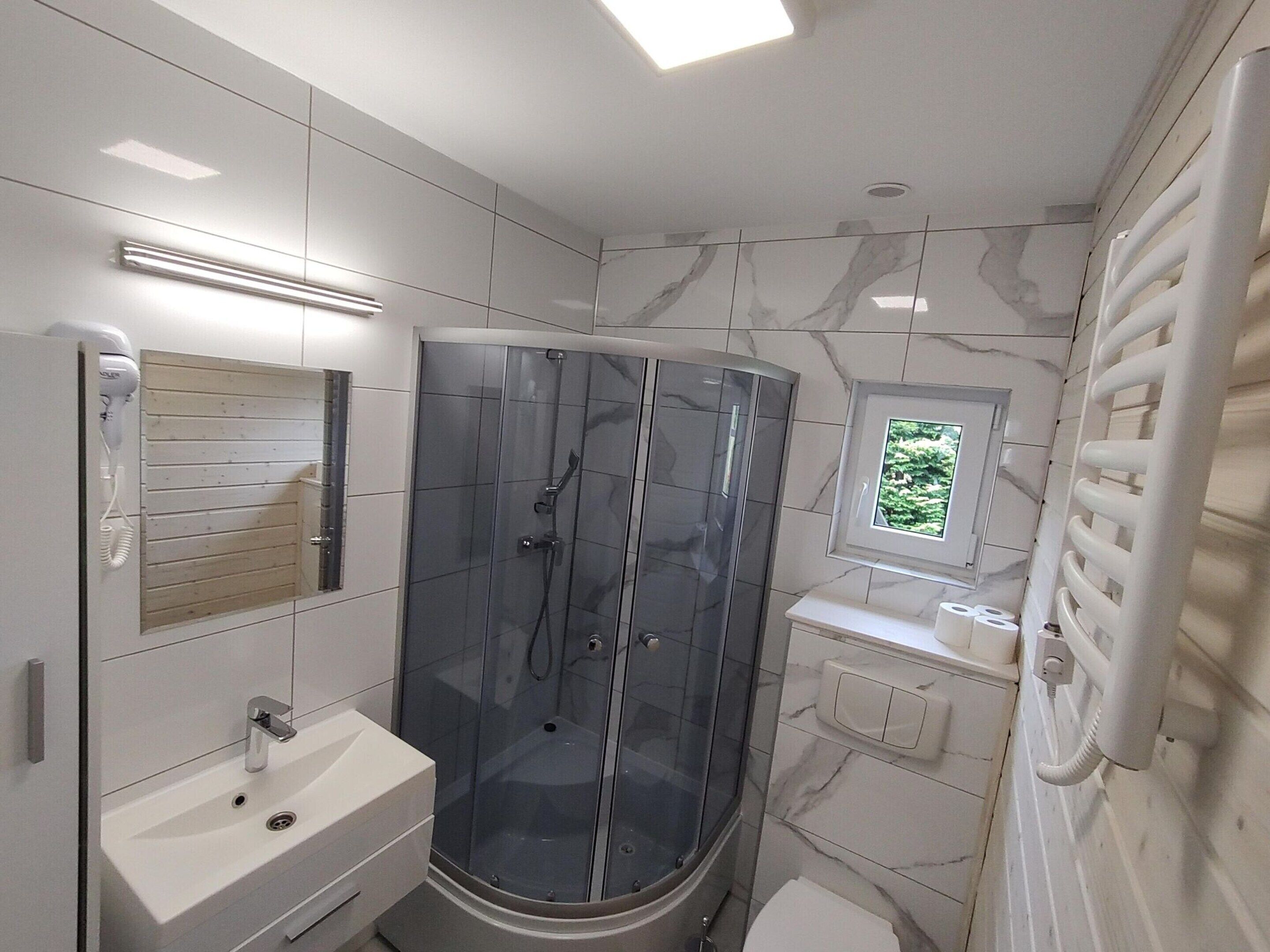 Un baño moderno con ducha envuelta en vidrio, un lavabo, un inodoro y un ventanal pequeño.