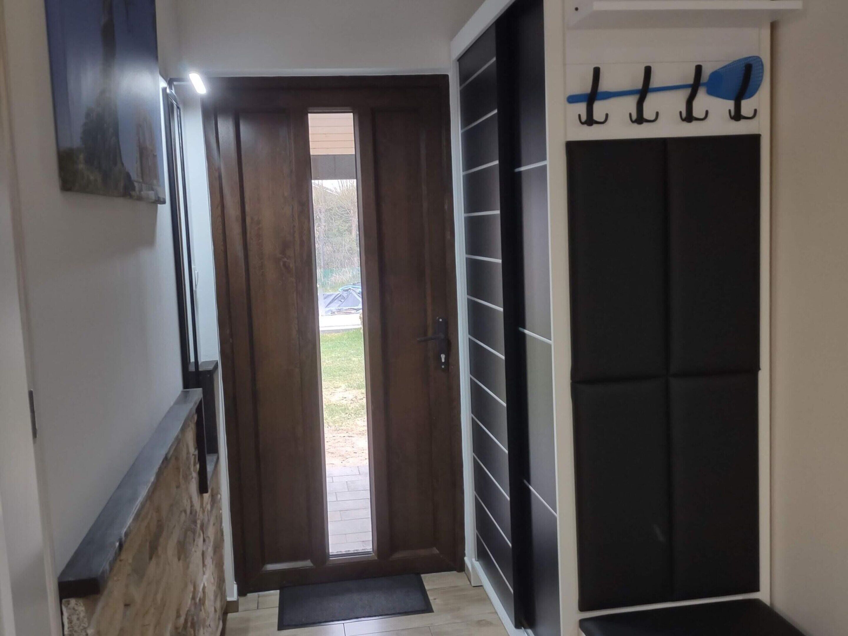 A hallway with a wooden door, a black sliding door, and a wall-mounted rack with items.