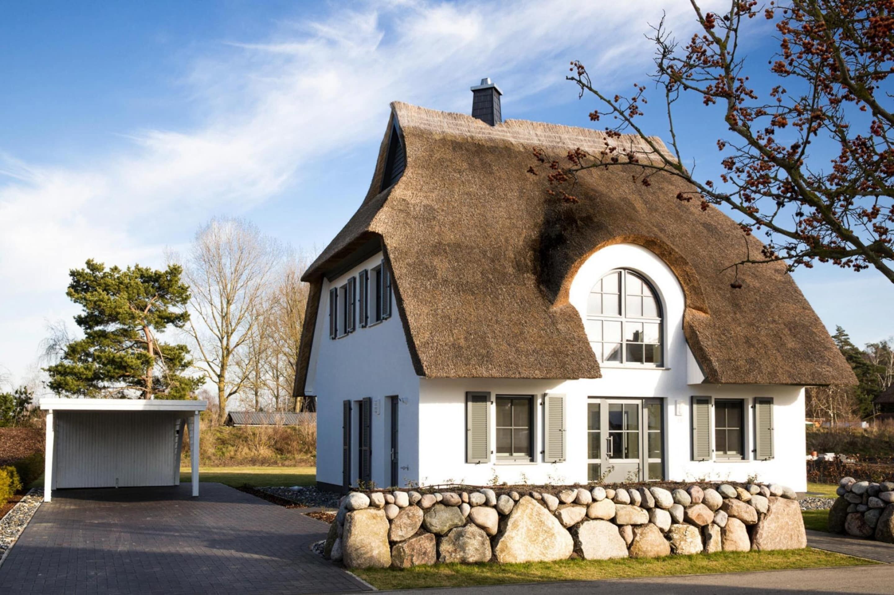 A white house with a thatched roof and stone foundation.