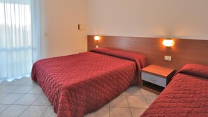 A hotel room with two beds, a nightstand, and a wall-mounted light fixture. - Apartment in Bibione Near the Beach (San Michele al Tagliamento)