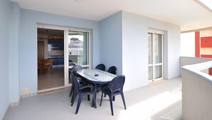 A balcony with a table and chairs, a sliding glass door leading to a kitchen, and a view of a building. - Apartment in Bibione Near the Beach (San Michele al Tagliamento)