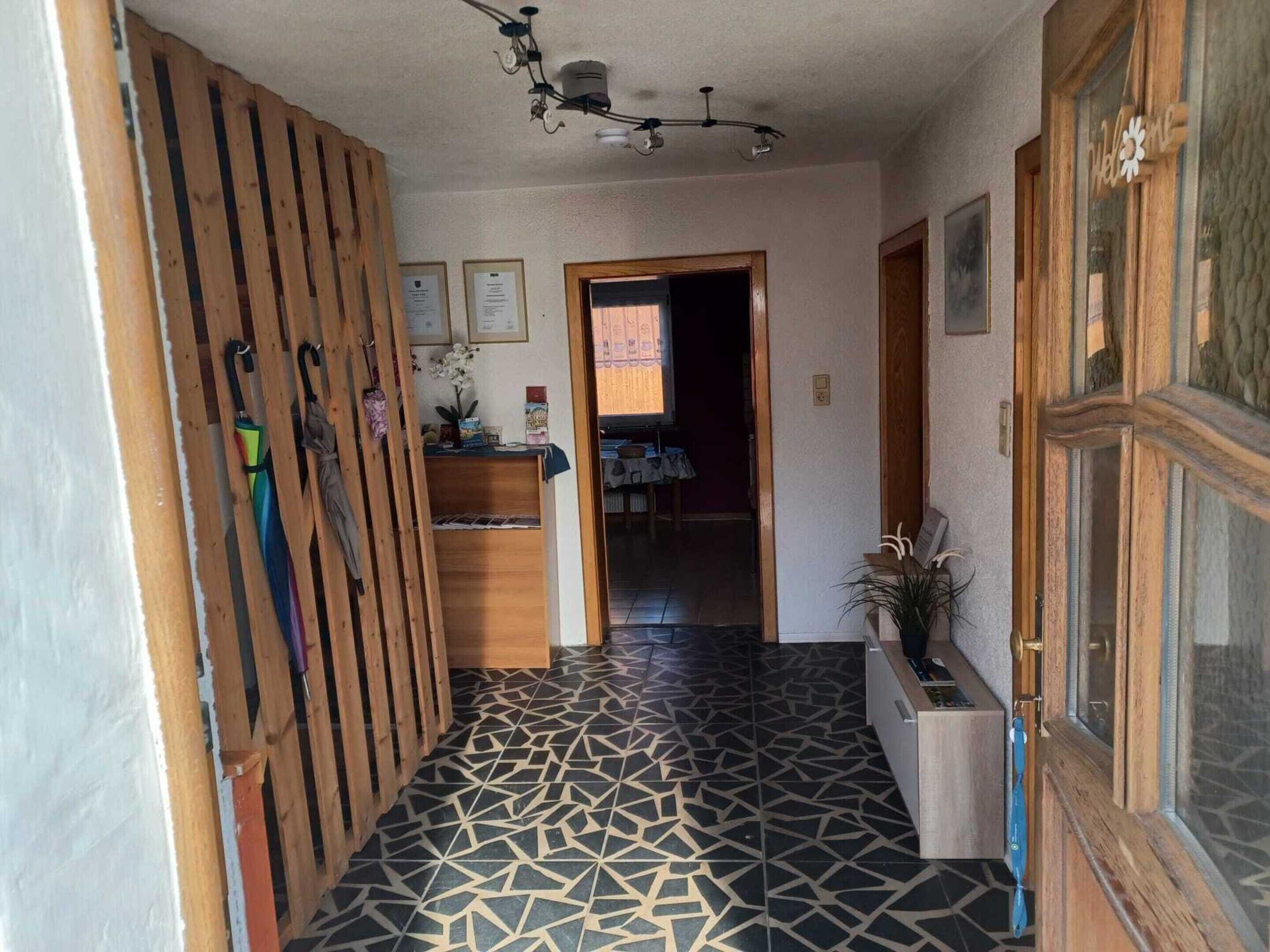 A hallway with patterned flooring, wooden slats, a ceiling light fixture, and a door with a 'Welcome' sign.