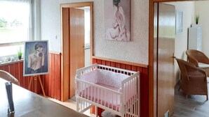 A baby room with a crib, wooden paneling, a painting on the wall, and wicker chairs. - Reihenhaus in Rhon Nahe Wasserkuppe (Kaltennordheim)