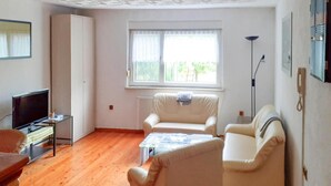 A living room with a sofa, a television, and a window with curtains. - Reihenhaus in Rhon Nahe Wasserkuppe (Kaltennordheim)