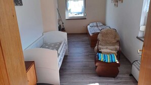 A room with a crib, a sofa, a chair, a window, and a radiator. - Reihenhaus in Rhon Nahe Wasserkuppe (Kaltennordheim)