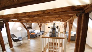 Un loft de concepto abierto con vigas de madera expuestas, una barandilla de madera central y una kitchenette al fondo.