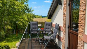 Eine Terrasse mit Außenbestuhlung, Blick auf die umliegende Natur und ein Gebäude mit Stein- und Backsteinfassade.