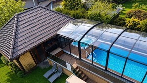 Ein von Glas umschlossener Pool mit Whirlpools, eine Holzterrasse und ein kleines Pavillon.