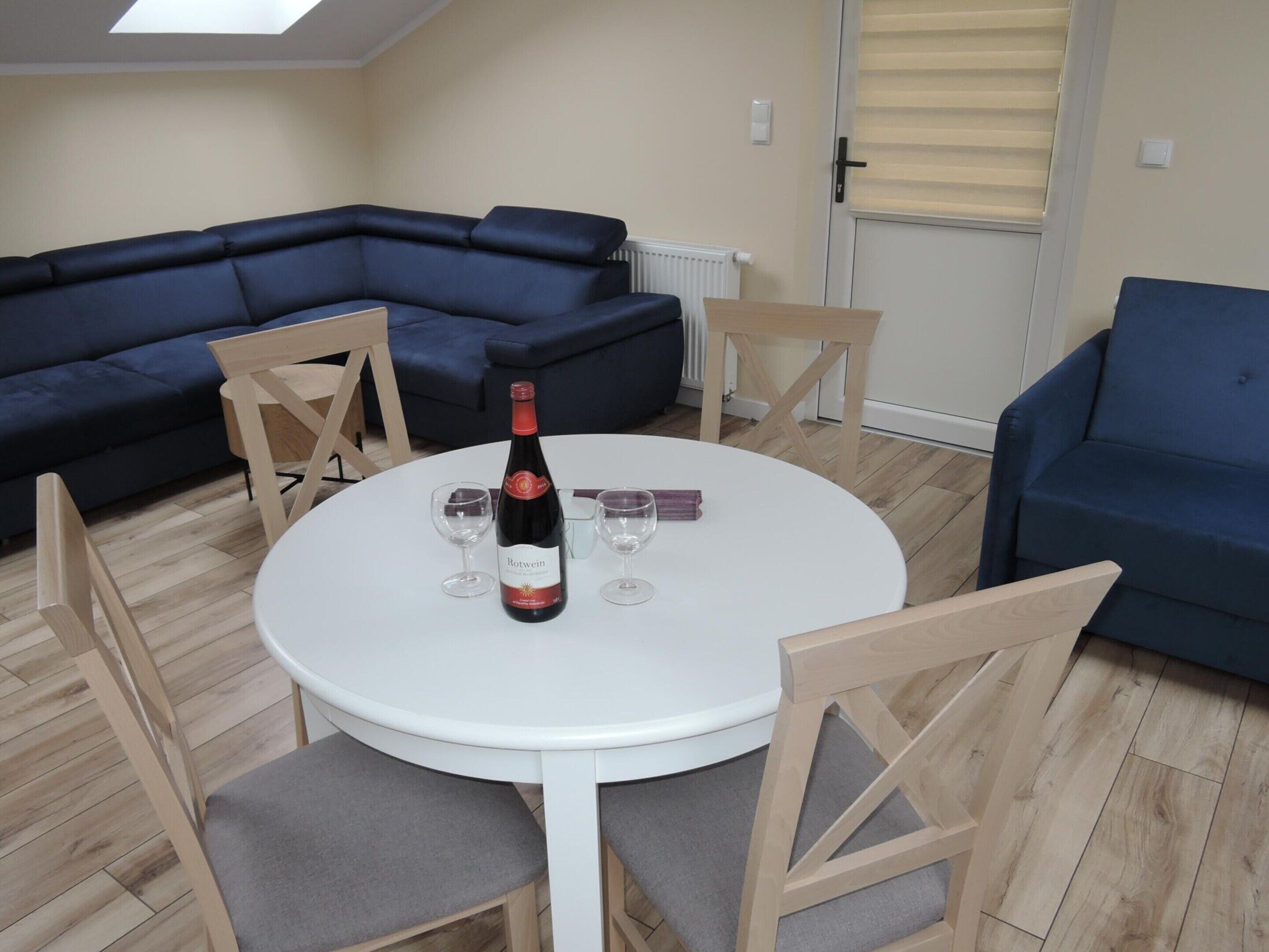 Een moderne woonkamer met een ronde witte tafel, twee blauwe banken en houten stoelen.
