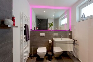 A modern bathroom with two toilets, a sink, and a shower. - Ferienhaus auf Usedom mit Garten und Hafenblick (Peenemünde)