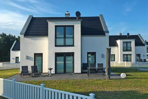 A modern two-story house with a flat roof, large windows, and a patio with outdoor furniture. - Ferienhaus auf Usedom mit Garten und Hafenblick (Peenemünde)