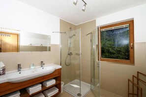 A bathroom with a glass-enclosed shower, a large mirror, and a window with a view of greenery. - Chalet in Zell am Ziller Near Ski Lifts (Rohrberg)