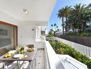 A balcony with a dining table set for two, a white railing, and a view of palm trees and a fence. - Pretty Apartment in Maspalomas Near the Beach-formerly TUI Ferienhaus (San Bartolomé de Tirajana)