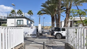 A gated entrance with a white fence, a paved pathway, and a white vehicle parked on the right. - Pretty Apartment in Maspalomas Near the Beach-formerly TUI Ferienhaus (San Bartolomé de Tirajana)