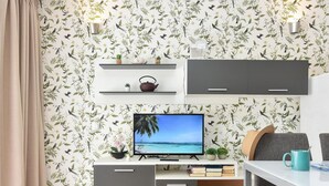 A modern living room with a TV, grey cabinets, a white table, and a floral wallpaper. - Pretty Apartment in Maspalomas Near the Beach-formerly TUI Ferienhaus (San Bartolomé de Tirajana)