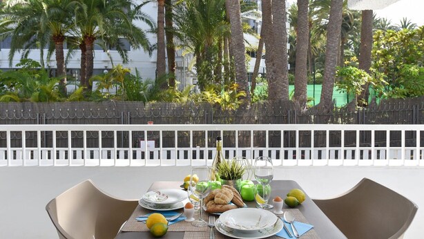A dining table set outdoors with a view of palm trees and a white fence. - Pretty Apartment in Maspalomas Near the Beach-formerly TUI Ferienhaus (San Bartolomé de Tirajana)