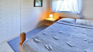 A bedroom with a bed, a nightstand with a lamp, a window with curtains, and a picture on the wall.