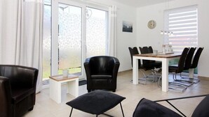 A modern living room with a dining area, featuring a sofa, a coffee table, a dining table with chairs, and a view through large windows. - Ferienhaus, Boiensdorf (Boiensdorf)