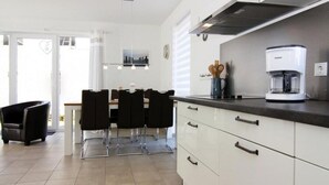 A modern kitchen with white cabinets, a coffee machine, and a dining area with a table and chairs. - Ferienhaus, Boiensdorf (Boiensdorf)