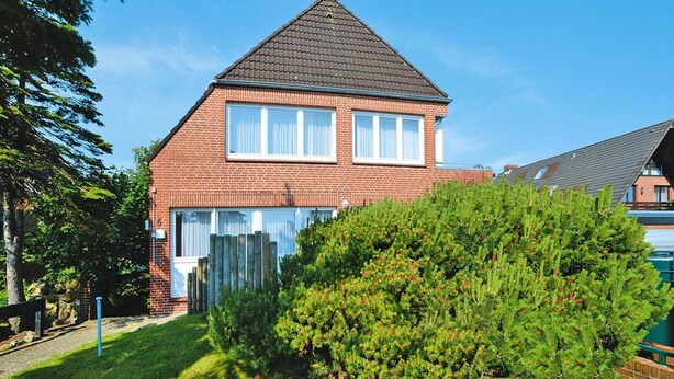 Een tweelaags bakstenen huis met een puntige dakkapel, het nummer '6' duidelijk zichtbaar aan de zijkant, en een verzorgd gazon met een grote naaldboom op de voorgrond.